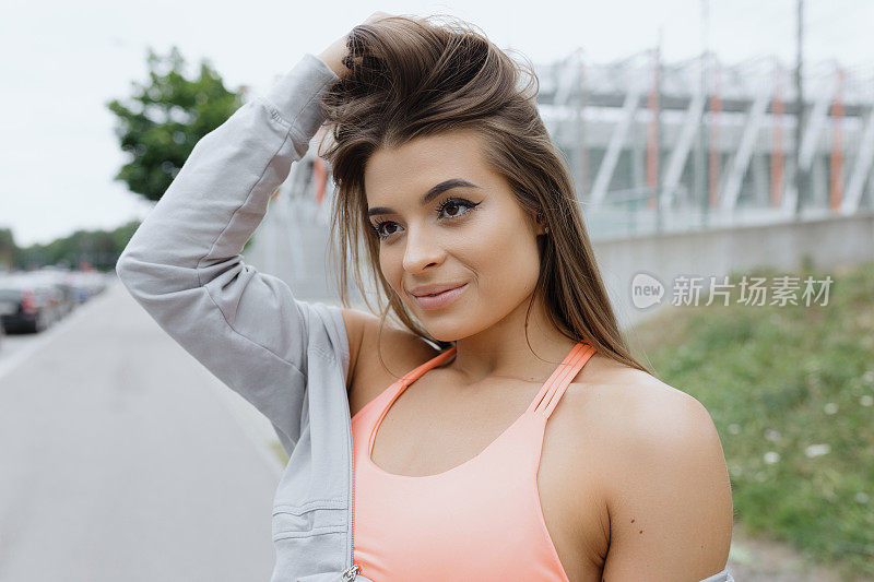 A woman with a sports bra is holding her hair in her hand, smiling happily